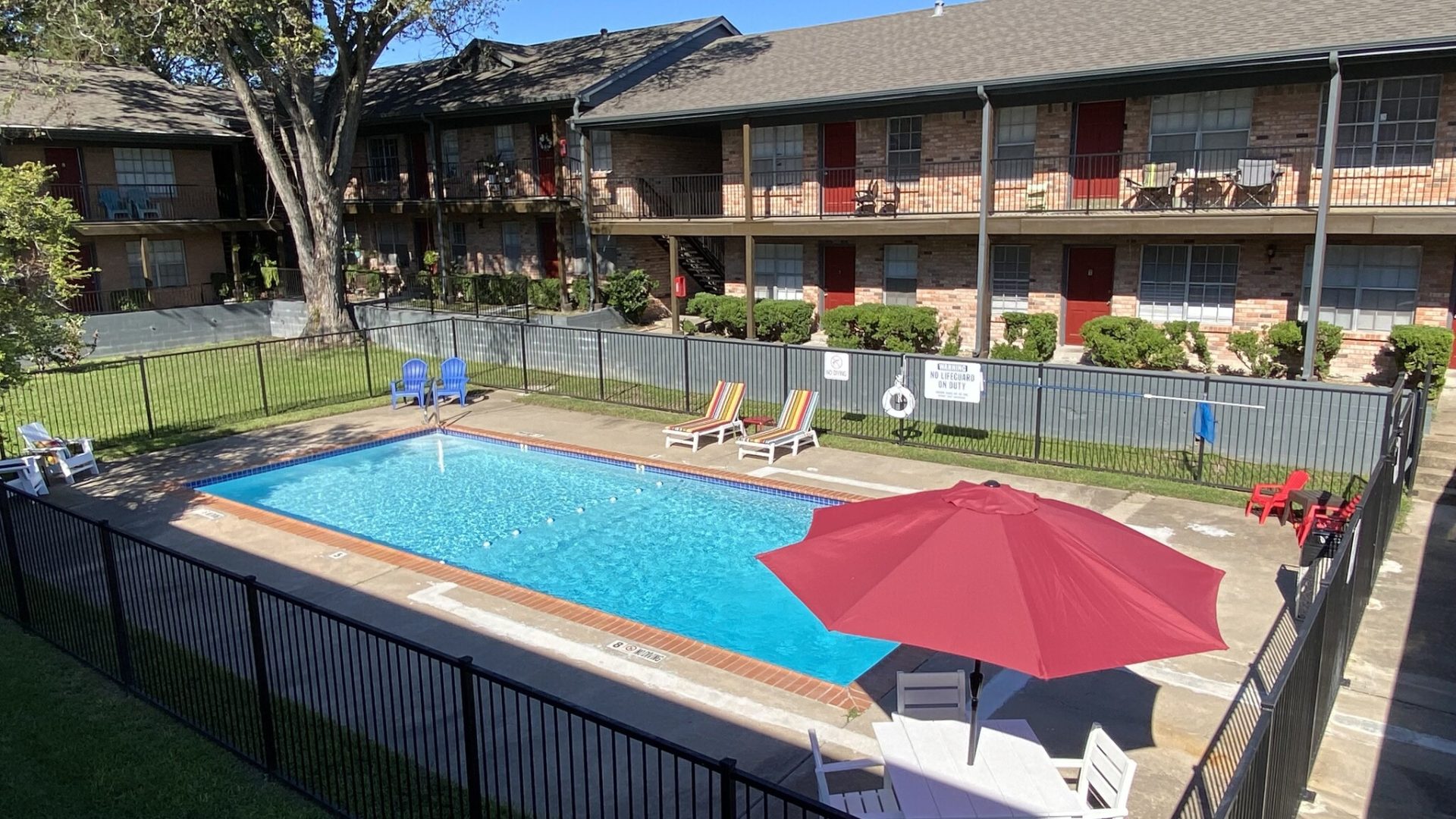 Sparking blue pool with red umbrella with comfortable outdoor seating in courtyard of the Claridge Apartments in Huntsville, TX.